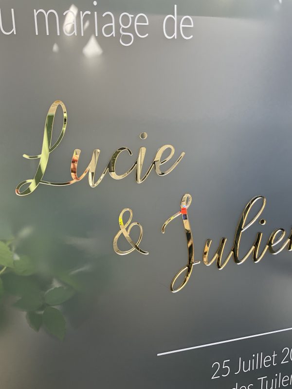 Cette photo représente un panneau de bienvenue en plexi givré avec les prénoms des mariés découpé dans du plexi doré mis en relief